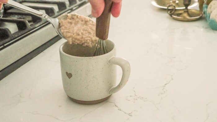 Hot oatmeal being tempered into a mug with eggs.