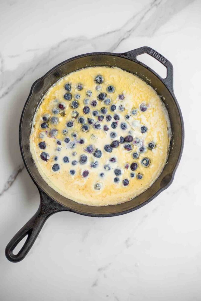 Blueberries scattered in a cast iron skillet with German pancake batter.