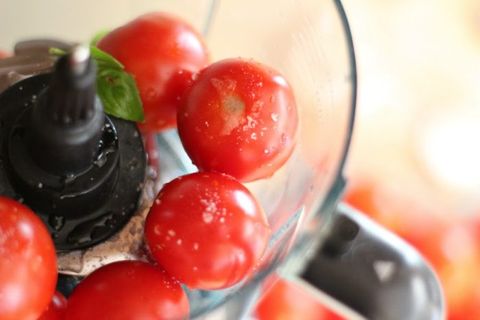 up close photo of tomatoes in a food processor with salt and basil