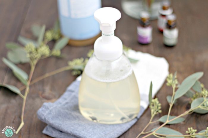 foaming hand soap in a bottle on a blue napkin with eucalyptus on each side and essential oils behind it.