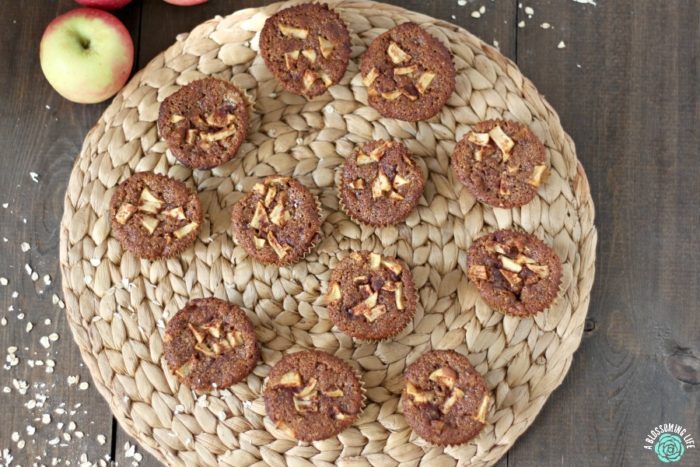 12 gluten free apple muffins on a rattan place pat with oars and apples surrounding it