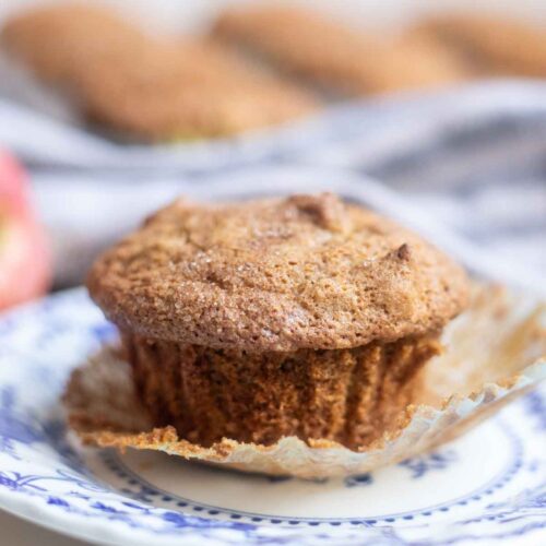Gluten free apple muffins on a blue and white plate with more muffins in the background.