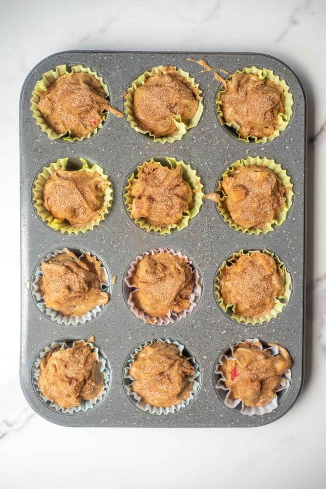 Apple muffin batter in a muffin tin topped with cinnamon sugar.