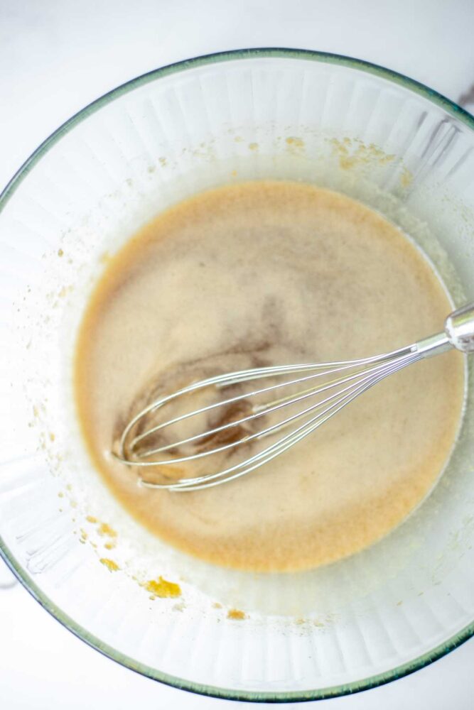 Eggs, butter, and sugar in a glass bowl with a whisk.