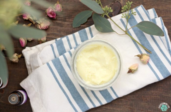 boo boo balm in a glass jar on a stripped cloth napkin. Dried roses and eucalyptus surround the jar