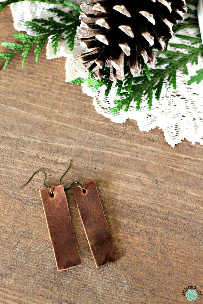 Pair of brown rectangular earrings laying on a table with pine cones on a while fabric doily behind it