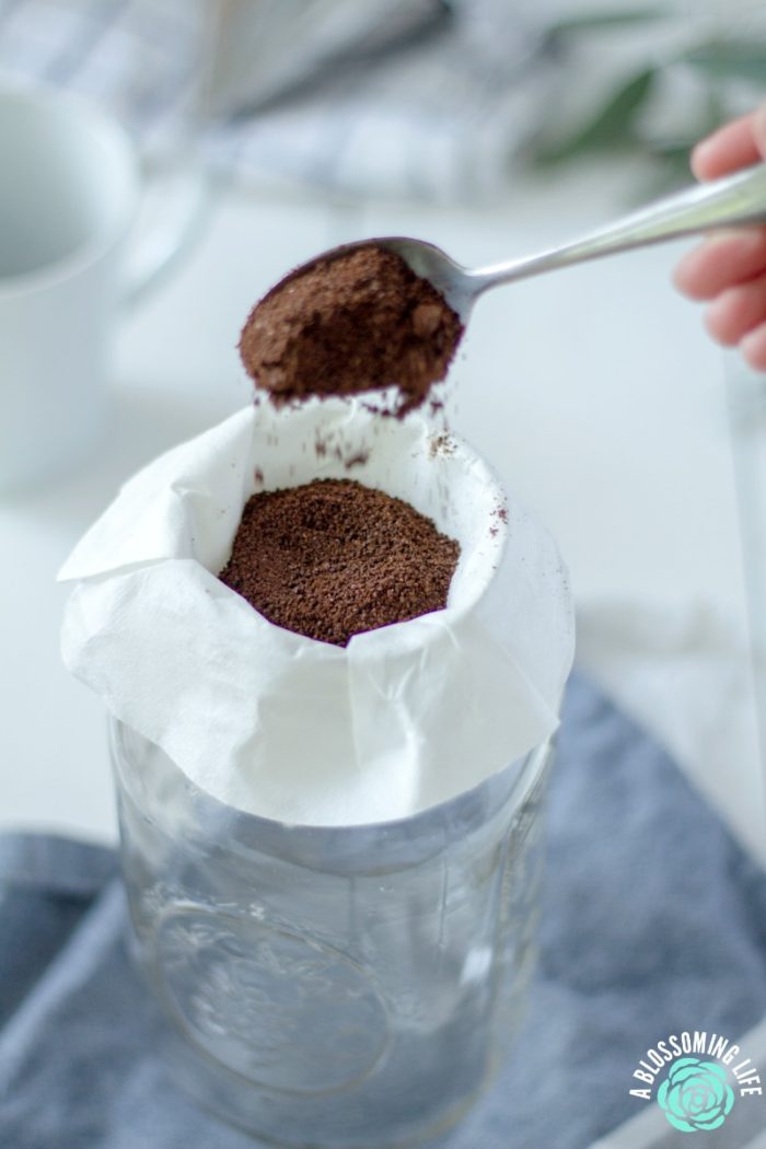 coffee grounds being poured into a coffee filter over a mason jar showing how to make coffee without a coffee maker