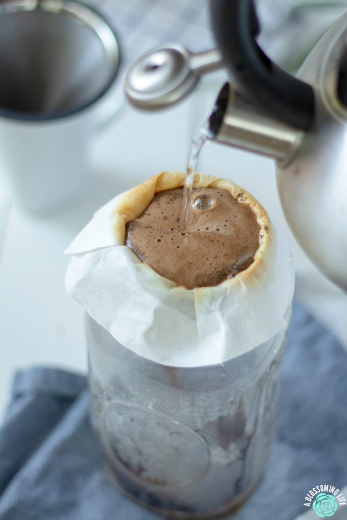 water from a tea kettle being poured into a coffee filter with coffee grounds 