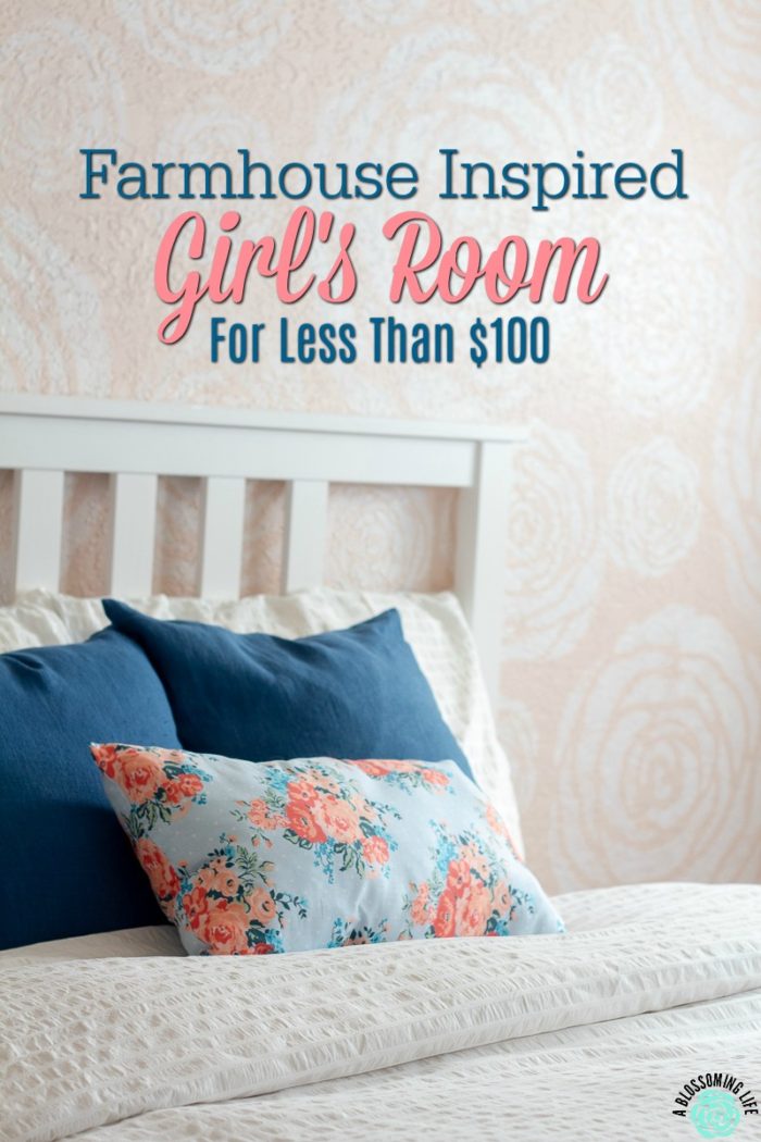 White stenciled flowers on a pink wall with a bed with white linens and blue pillows