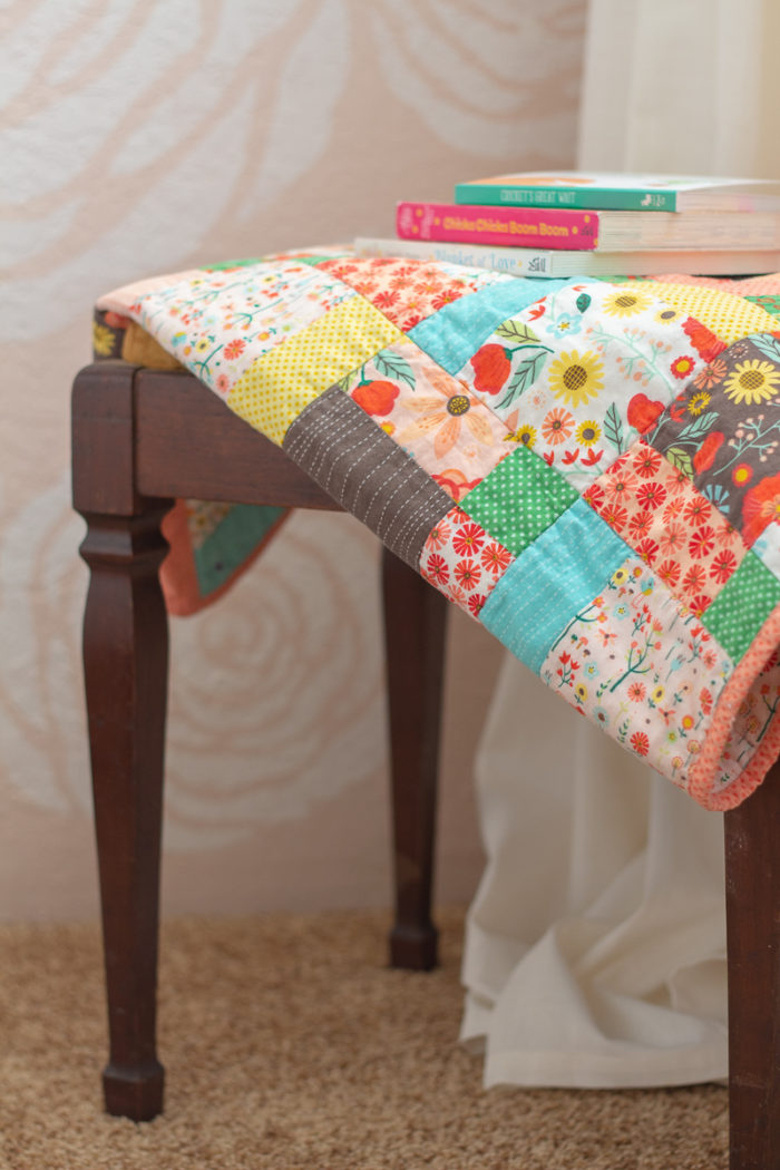 antique bench topped with handmade quilt and kid books in front of DIY stenciled flower wall