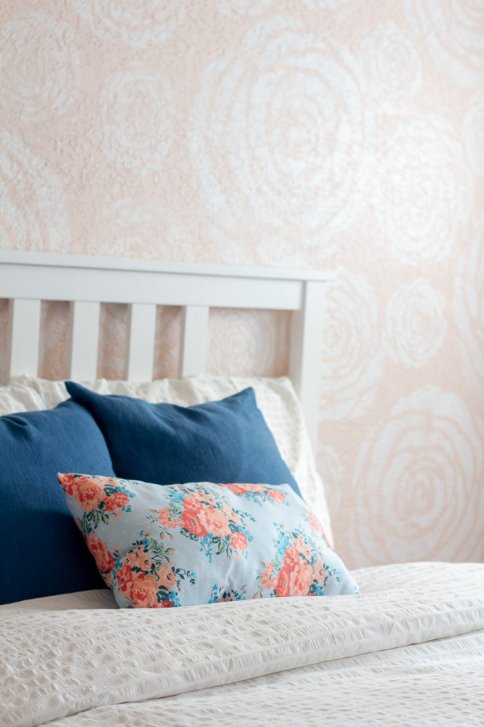 DIY stenciled flowers on a wall with a bed in front with white linens and blue pillows