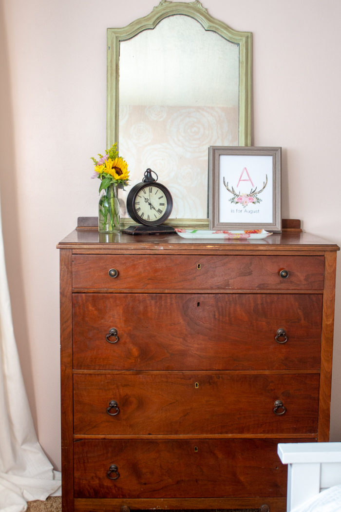 antique dresser topped with fresh flowers, clock, picture and antique green mirror.