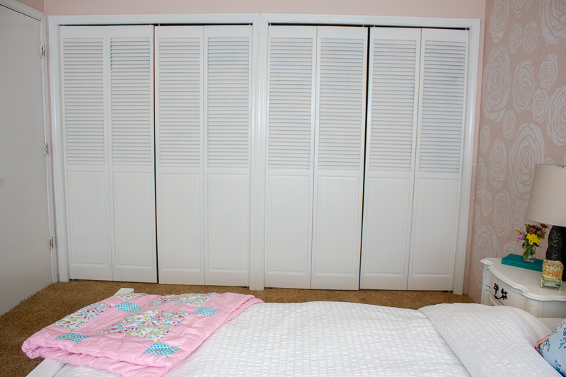 white closet doors surrounded by white trim and pink painted walls. Also part of the bed is shown