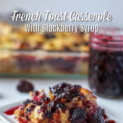 Slice of French Toast Casserole with Blackberries covered with blackberry syrup and a baking dish and jar of blackberry syrup in the back