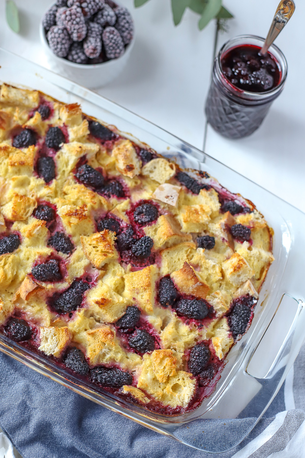 Baked french toast casserole with blackberries and maple blackberry syrup in a glass jar.