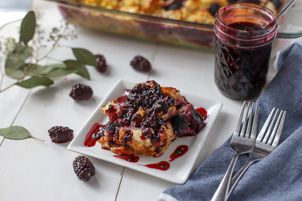Slice of French Toast Casserole with Blackberries covered with blackberry syrup and a baking dish in the back