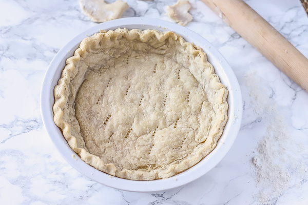 Baked gluten free pie crust in a white pie pan setting on a marble counter with extra dough and a rolling pin.
