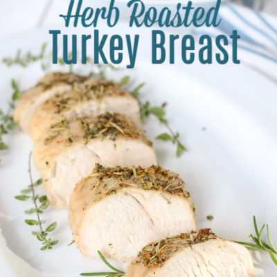 herb roasted turkey breast on a white plate with herbs around it.