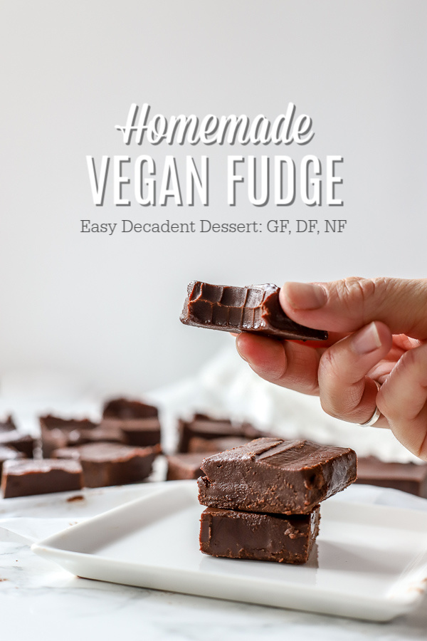Vegan fudge stacked 3 tall on a white plate. Hand holding one piece of vegan fudge with a bite taken out. More pieces of fudge in the background