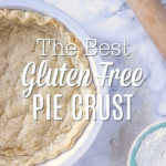 Gluten Free Pie Crust in a pie pan laying on a marble counter with a rolling pin and bowl of gluten free flour