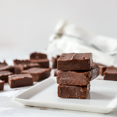 cegan fudge stacked up 3 tall on a white plate with more pieces of fudge behind it