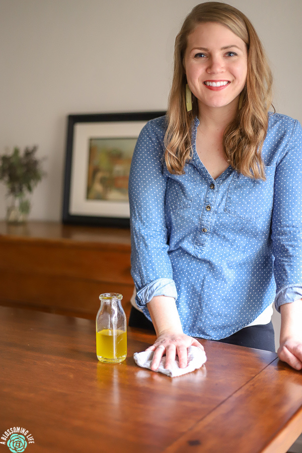 women in a blue shirt using homemade furniture polish to polish wooden table