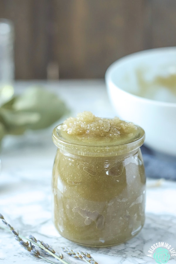 sugar scrub in a glass jar on marble counter with lavender in front and white bowl behind