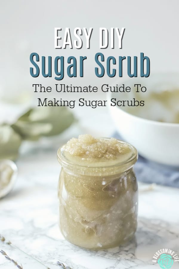 jar of sugar scrub on a marble countertop with an bowl of scrub behind it and dried eucalyptus