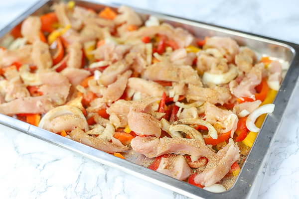 raw chicken, peppers, onions, and seasonings on a sheet pan to make sheet pan chicken fajitas