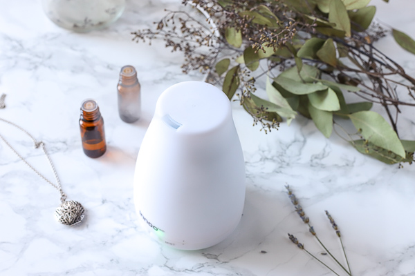 White essential oil diffuser with essential oils and eucalyptus behind it