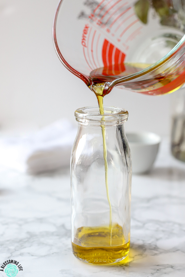 pouring olive oil into a glass bottle to make homemade furniture polish