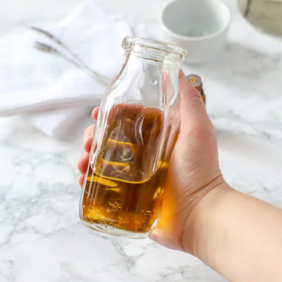 glass bottle of homemade furniture polish with marble counter and white bowls behind it