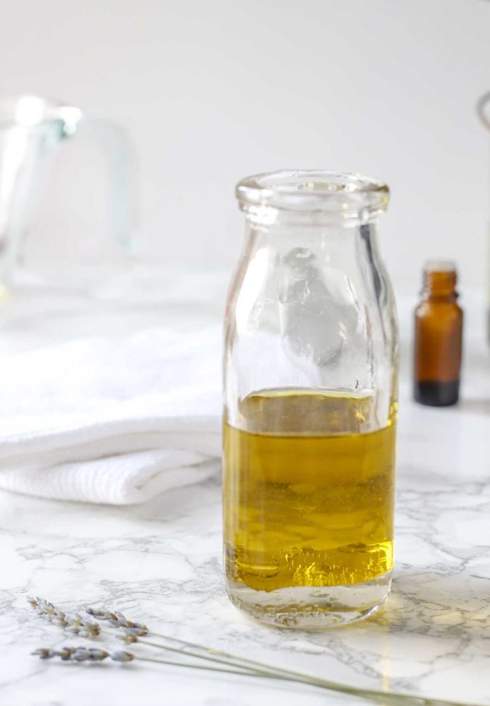 glass bottle of homemade furniture polish on a white countertop with essential oils and cloths in the background and dried lavender in the front
