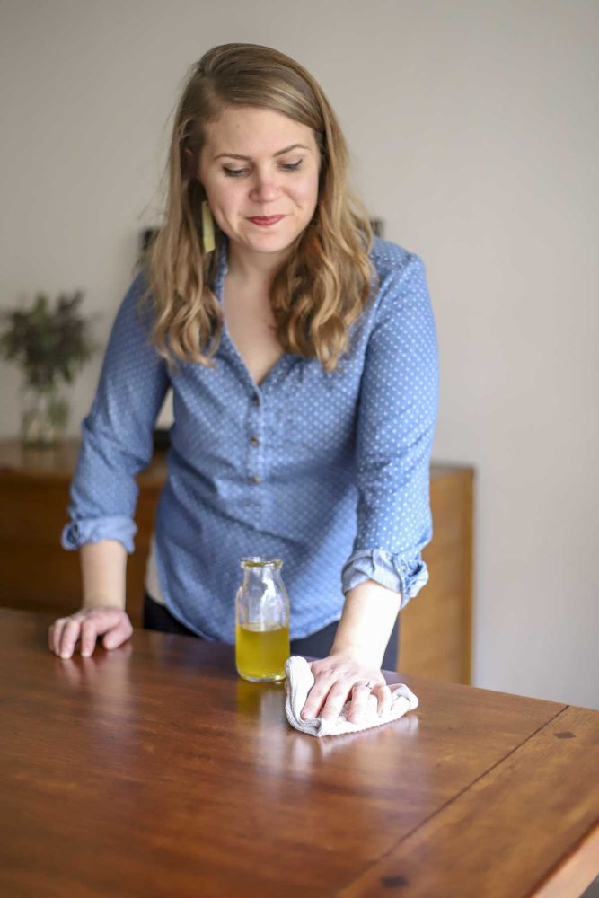 woman using DIY furniture polish with a white cloth on a wood table