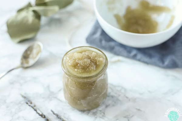 clear glass jar of sugar scrub on a marble countertop with an bowl of scrub behind it and dried eucalyptus