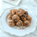 vegan truffles stacked up on a white scalloped plate on a marble counter