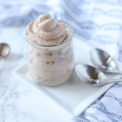 chocolate whipped cream in a glass container on a white plate with silver spoons