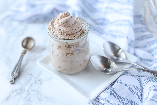 chocolate whipped cream in a glass container on a white plate with silver spoons