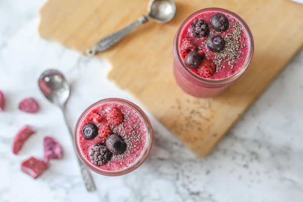 overhead shot of two berry beet smoothies topped with frozen berries and chia seeds on top a marble counter and wood cutting board