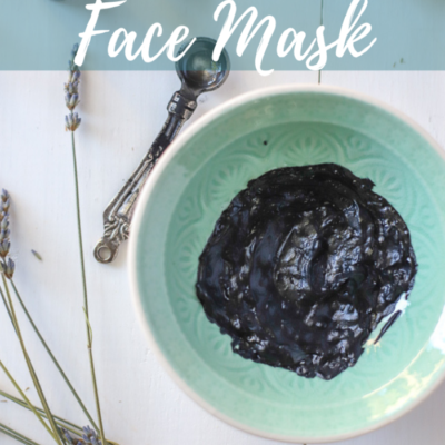 DIY charcoal face mask in a teal dish with dried lavender and measuring spoons around it