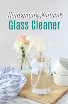 natural homemade glass cleaner in a glass bottle on a wood cutting board with a blue and white napkin and jars behind it