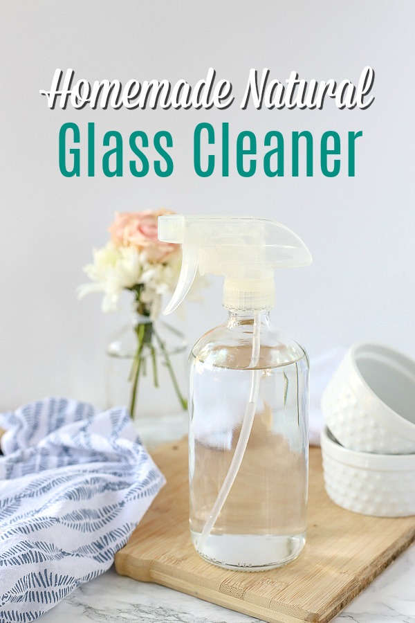 natural DIY glass cleaner in a glass bottle on a wood cutting board with a blue and white napkin and jars behind it