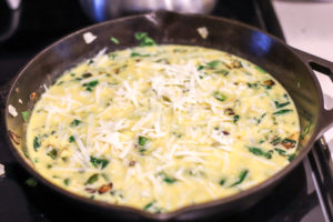 cast iron skillet with eggs, spinach, green peppers and topped with cheese for a spinach frittata