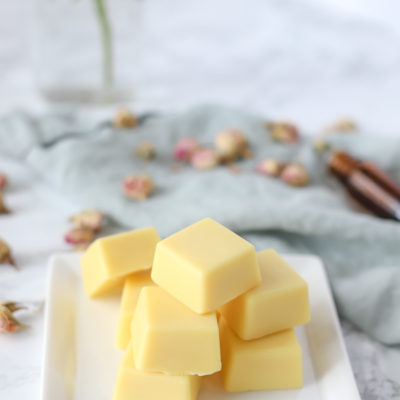 DIY lotion bar on a white place with essential oils and dried roses behind it