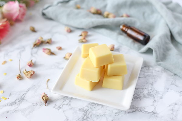 lotion bars on a white plate with dried herbs and essential oils behind it