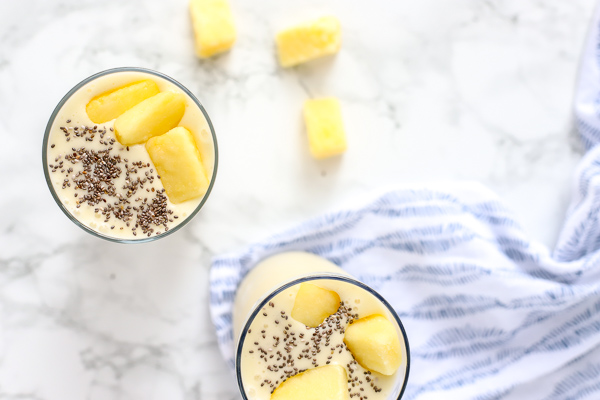 two pina colada smoothies topped with chia seeds and pineapple on a blue and white napkin