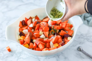 adding oil, herbs and garlic to a bowl of root vegetables for roasted root vegetable recipe