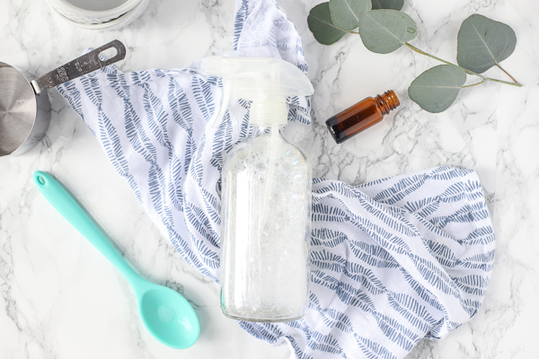 Homemade stain remover in a glass bottle on a blue and white napkin with a teal spoon and essential oil bottle next to it