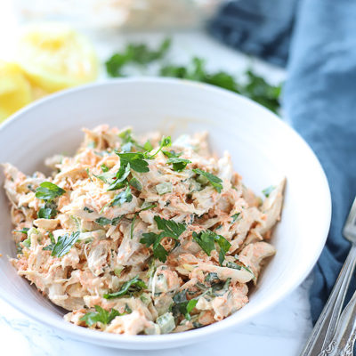 healthy chicken salad in a white bowl with lemons behind it