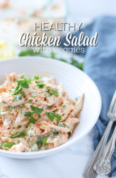 healthy chicken salad in a white bowl on top a blue napkin with antique forks to the right